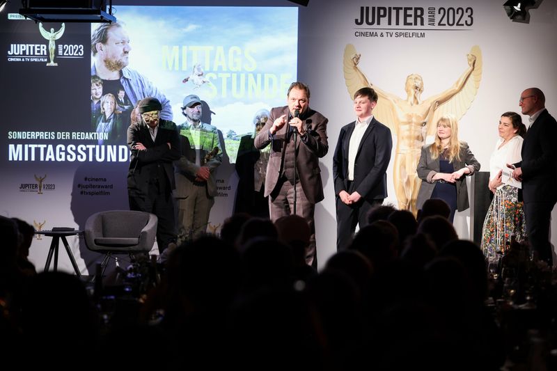 Charly Hübner (M), Schauspieler, und das Team von "Mittagsstunde" stehen bei der Verleihung des Jupiter Award 2023 auf der Bühne. 