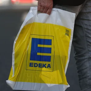 Ein Mann trägt eine Tüte der Supermarkt-Kette Edeka bei sich