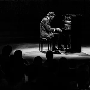Mann sitzt am Klavier auf der Bühne, vorne Köpfe des Publikums