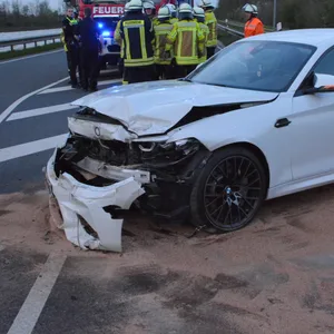 Der demolierte BMW. Im Hintergrund: Einsatzkräfte der Feuerwehr.