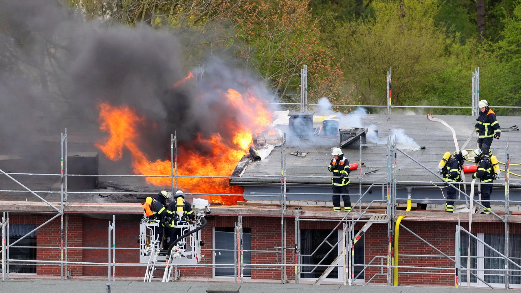 Feuerwehrleute löschen einen ausgedehnten Brand auf dem Dach eines Mehrfamilienhauses