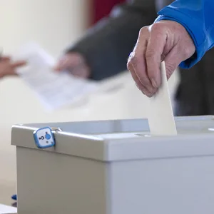 Ein Wähler steckt in einem Wahlbüro ein Wahlumschlag in eine Wahlurne (Symbolbild)