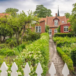 Ein Haus mit üppigem Garten, im Hintergrund ist ein Kirchturm zu sehen