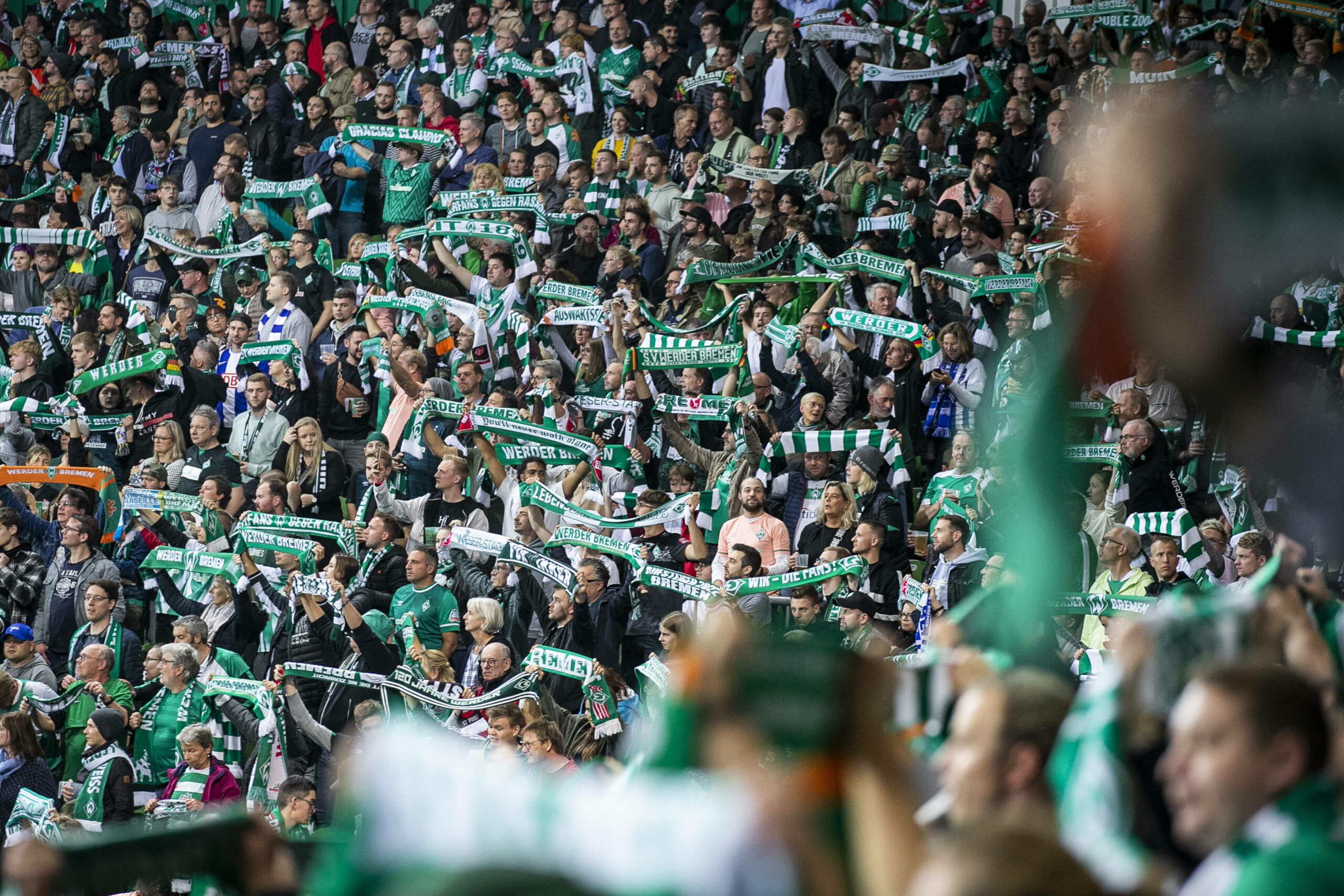 Fans des SV Werder Bremen halten ihre Schals hoch.