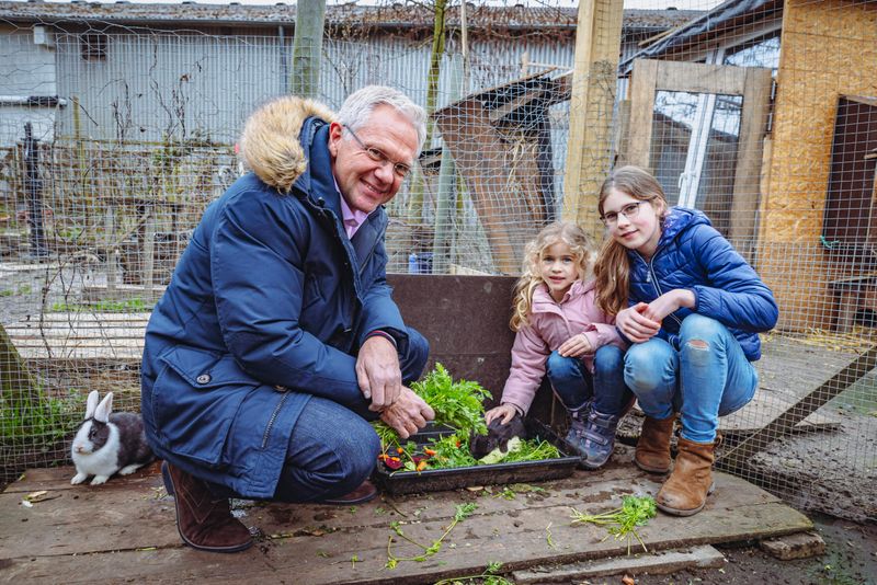 Norbert Zobel, Filialleiter der Haspa Rellingen, lässt sich von Kindern den Garten zeigen – im Kaninchengehege wird gefüttert.