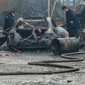 Ermittler untersuchen ein Fahrzeug neben einer Brandruine.