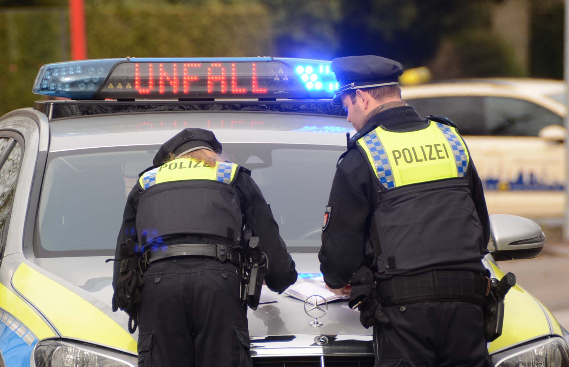 Zwei Polizisten sehen sich Papiere an, die auf der Motorhaube ihres Fahrzeugs liegen.