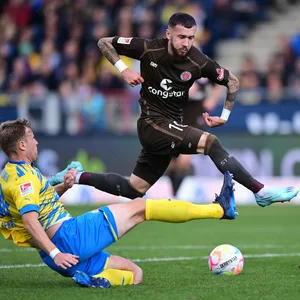 Marcel Hartel vom FC St. Pauli springt über das ausgestreckte Bein des Braunschweigers Brian Behrendt