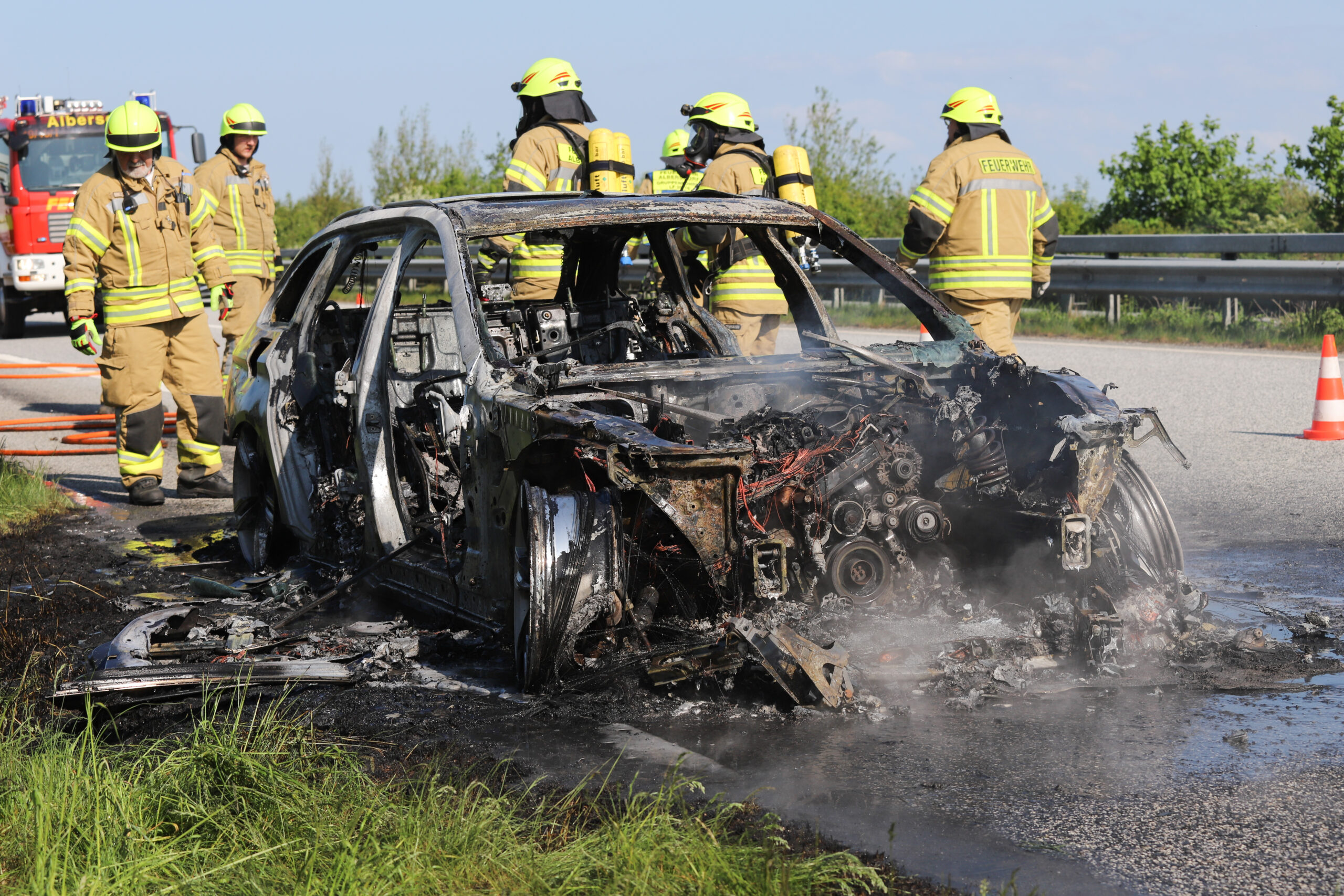 Der ausgebrannte Wagen steht auf dem Standstreifen, im Hintergrund Einsatzkräfte der Feuerwehr.