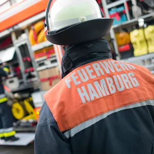 Einsatzkraft der Hamburger Feuerwehr steht mit dem Rücken zu der Kamera in Richtung eines Löschfahrzeugs.