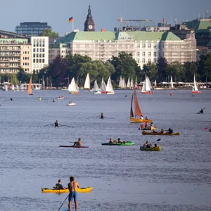 Menschen sind in der Abendsonne mit Stand-Up Boards, Kanus, Ruderbooten und Segelbooten auf der Alster unterwegs.