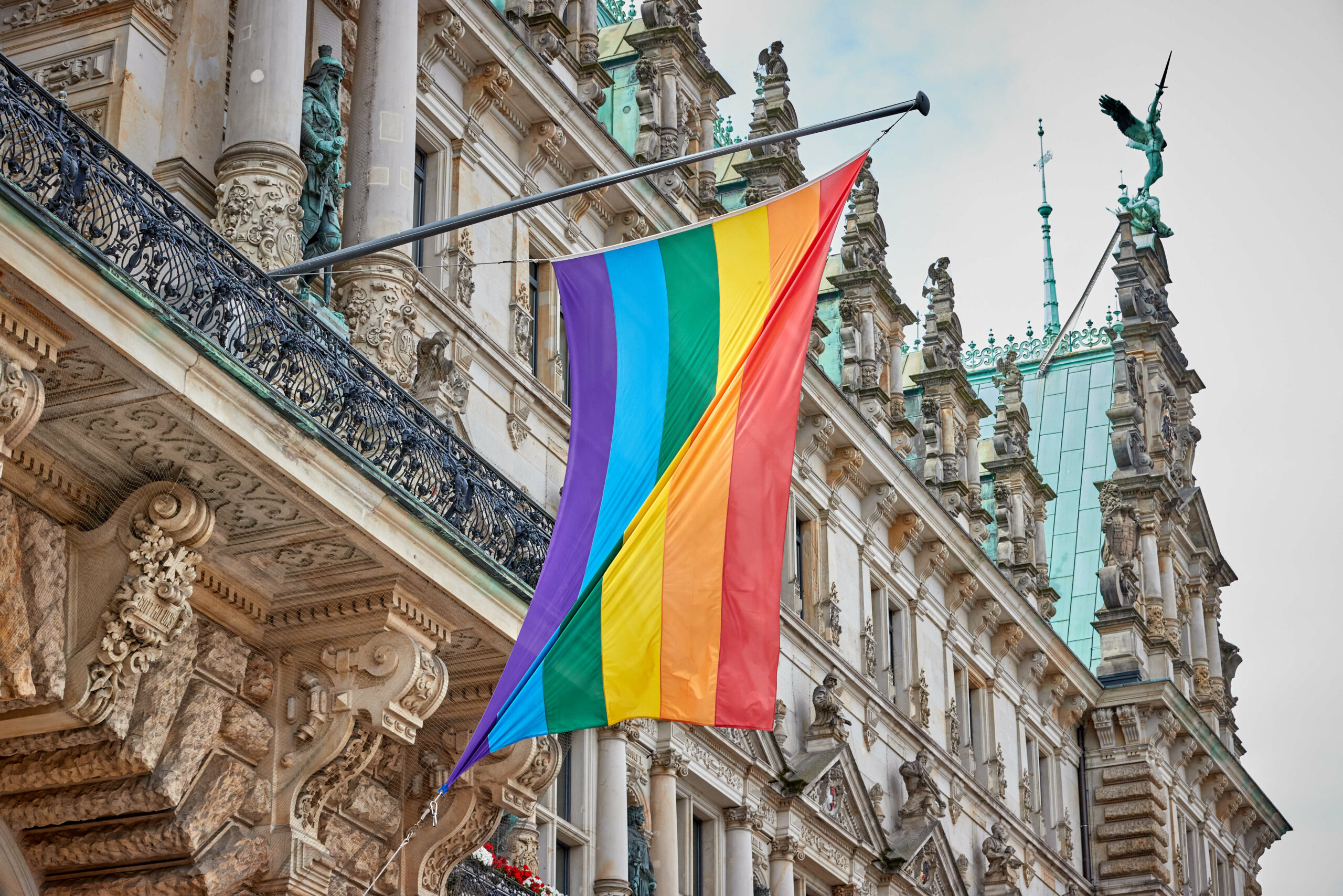Eine Regenbogenflagge hängt über dem Eingang des Hamburger Rathauses.