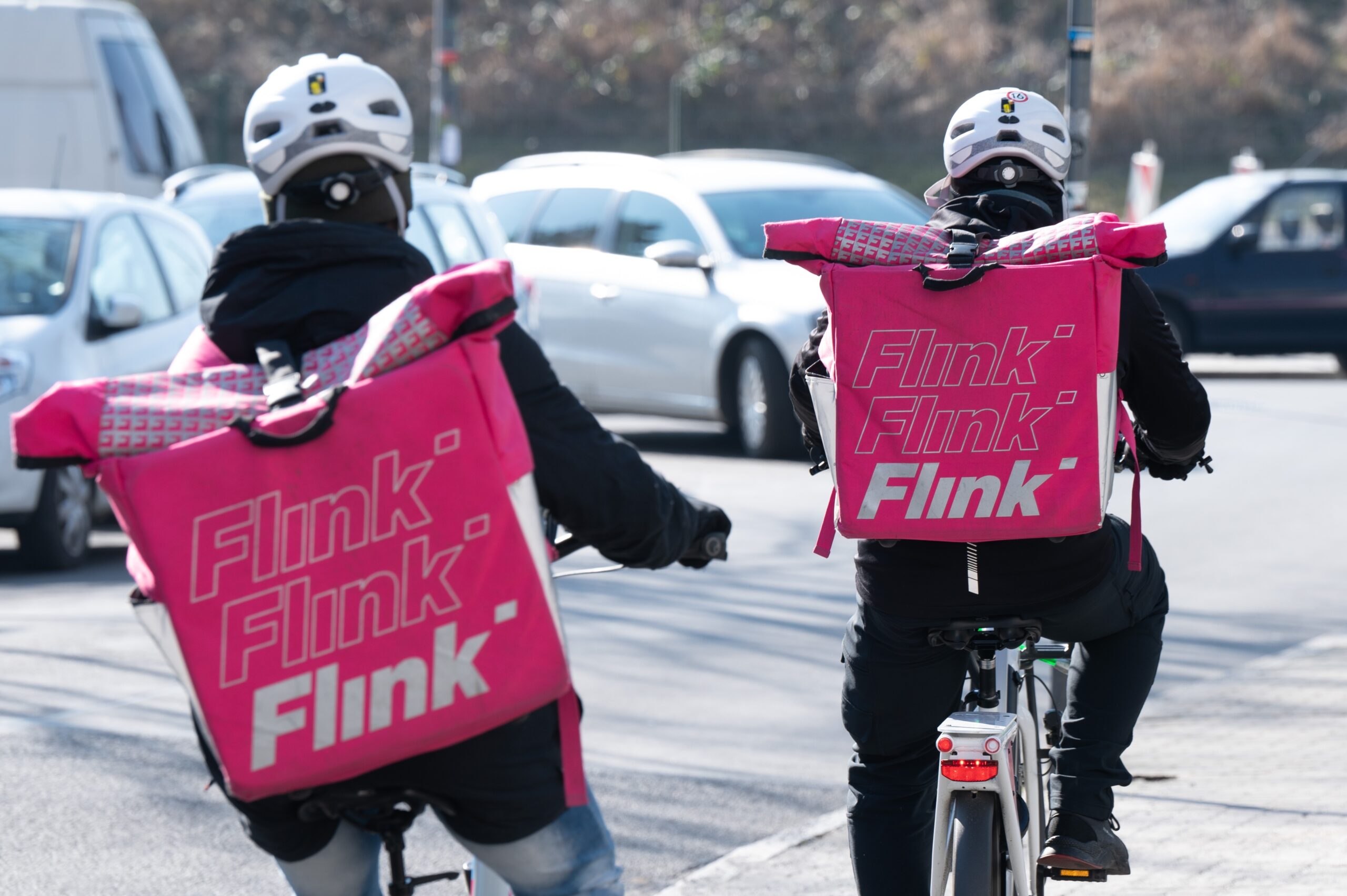 Zwei Fahrradkuriere tragen Rucksäcke mit dem Logo des Lebensmittel Lieferdienstes Flink