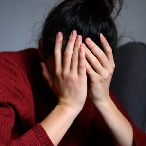 Eine Frau sitzt mit dem Kopf in den Händen auf einem Stuhl.