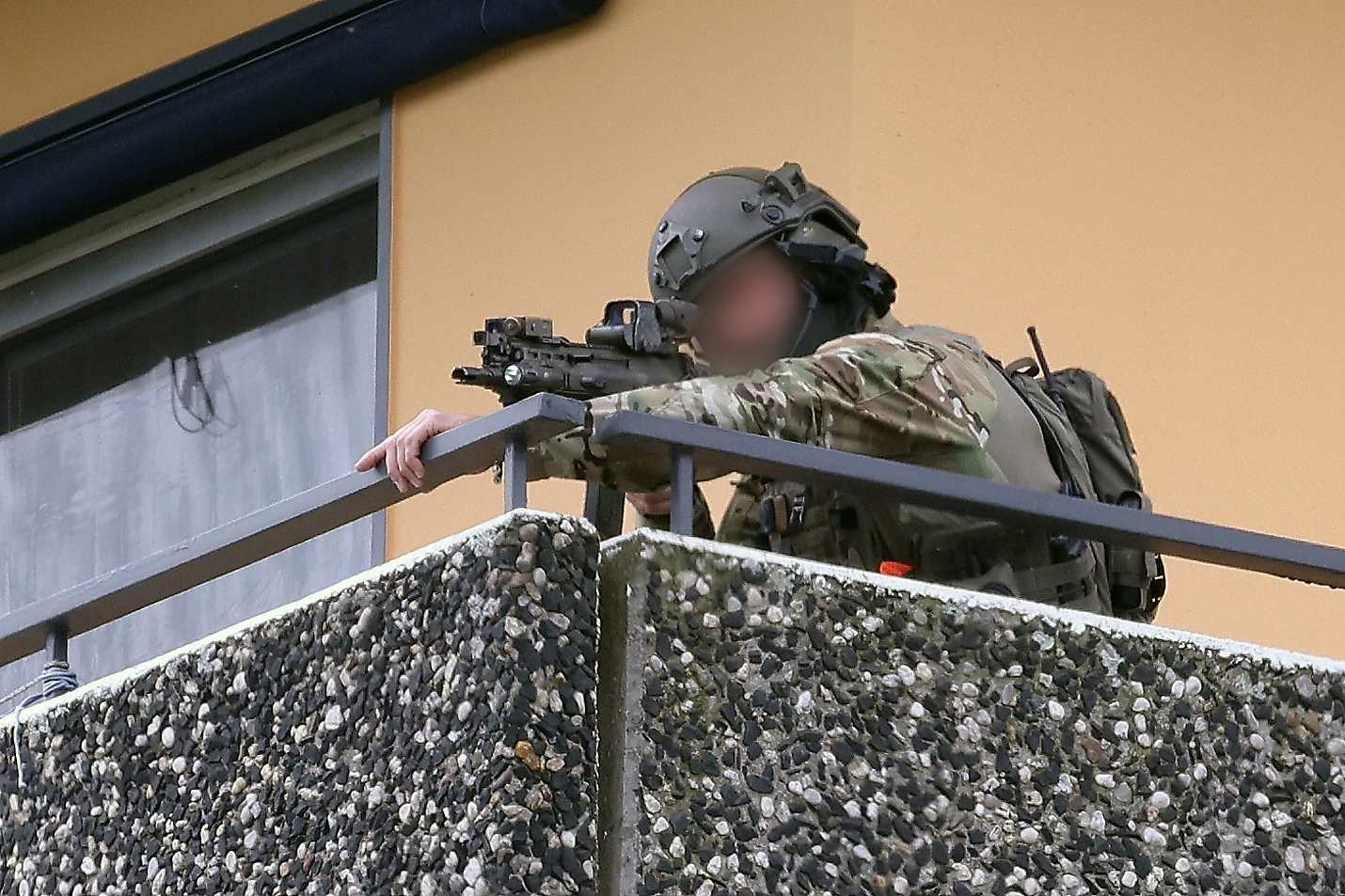 Ein Polizeibeamter in Spezialausrüstung steht auf einem Balkon und zielt mit seiner Waffe.
