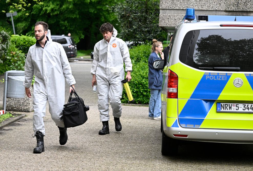 Zwei Männer in weißen Overalls laufen an einem Polizeiauto vorbei