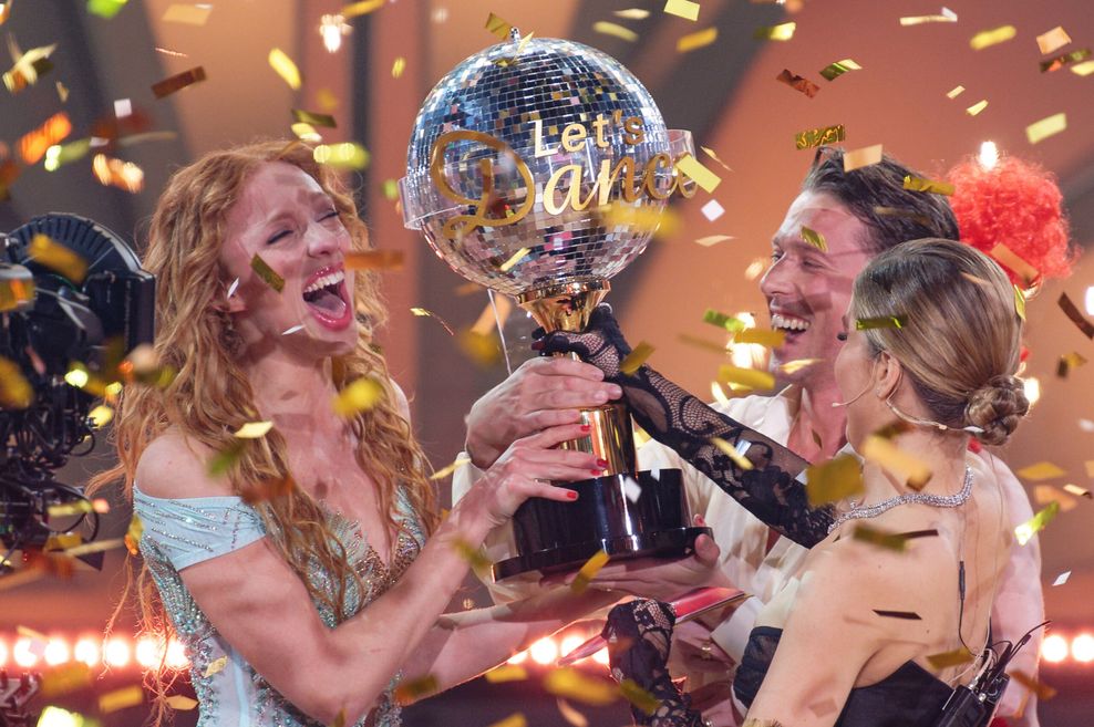 Model Anna Ermakova (l) und ihr Profi-Tanzpartner Valentin Lusin jubeln neben Victoria Swarovski, Moderatorin, über ihren Sieg mit der Trophäe nach dem Finale.