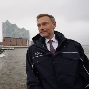 Christian Lindner (FDP), Bundesminister der Finanzen, steht an Deck des Zollbootes „Kehrwieder“ während einer Fahrt durch den Hamburger Hafen. Im Hintergrund ist die Elbphilharmonie zu sehen.