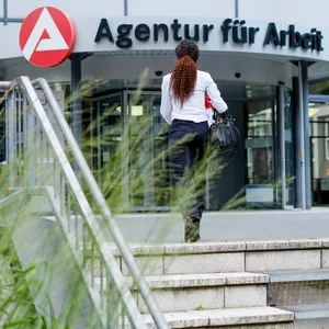 Eine Frau geht auf den Eingang der Agentur für Arbeit zu.