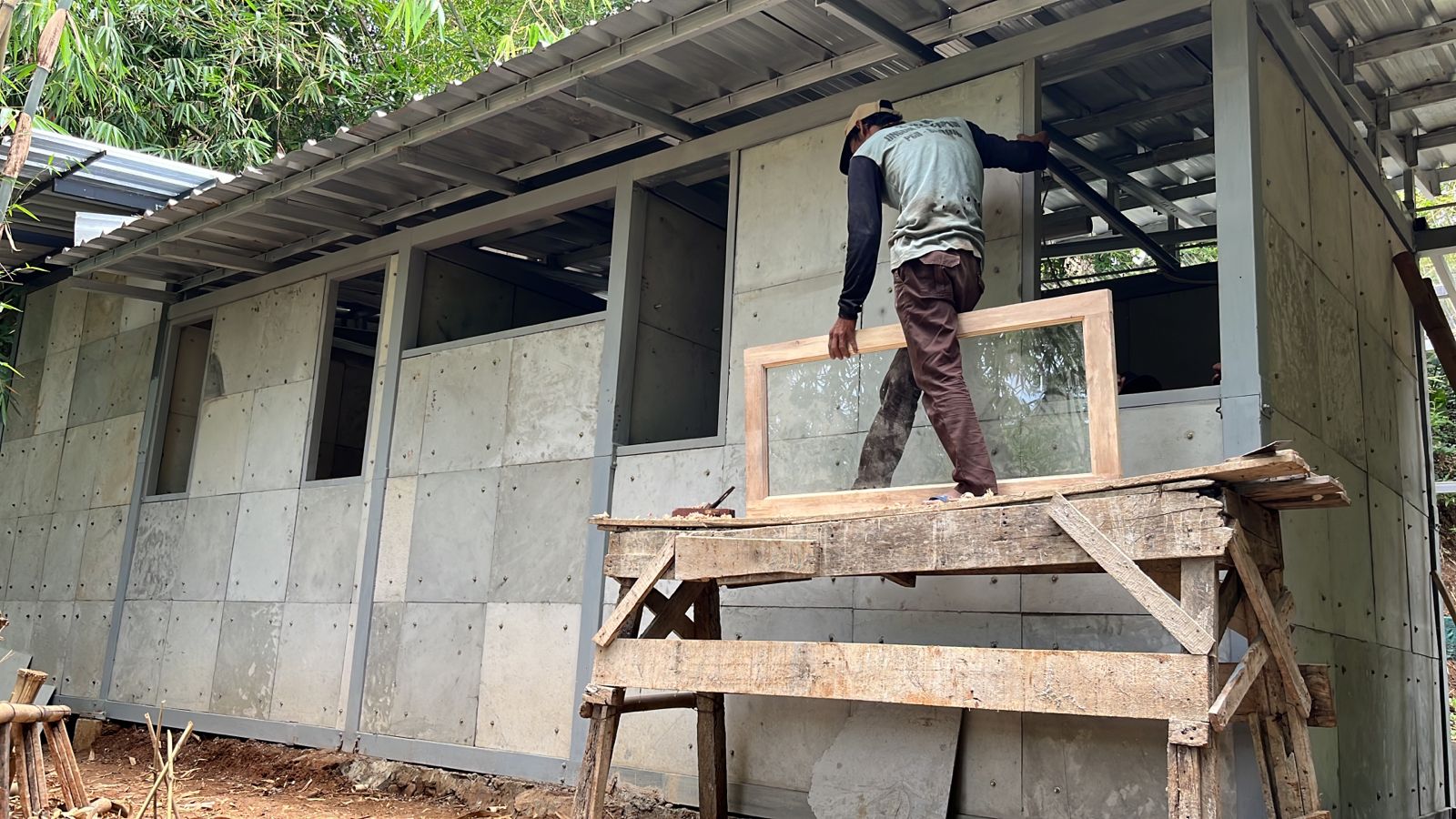 Ein Mann arbeitet am Rohbau eines einfachen Hauses, bei dem gebrauchte Windeln einen Teil des Baumaterials ersetzen