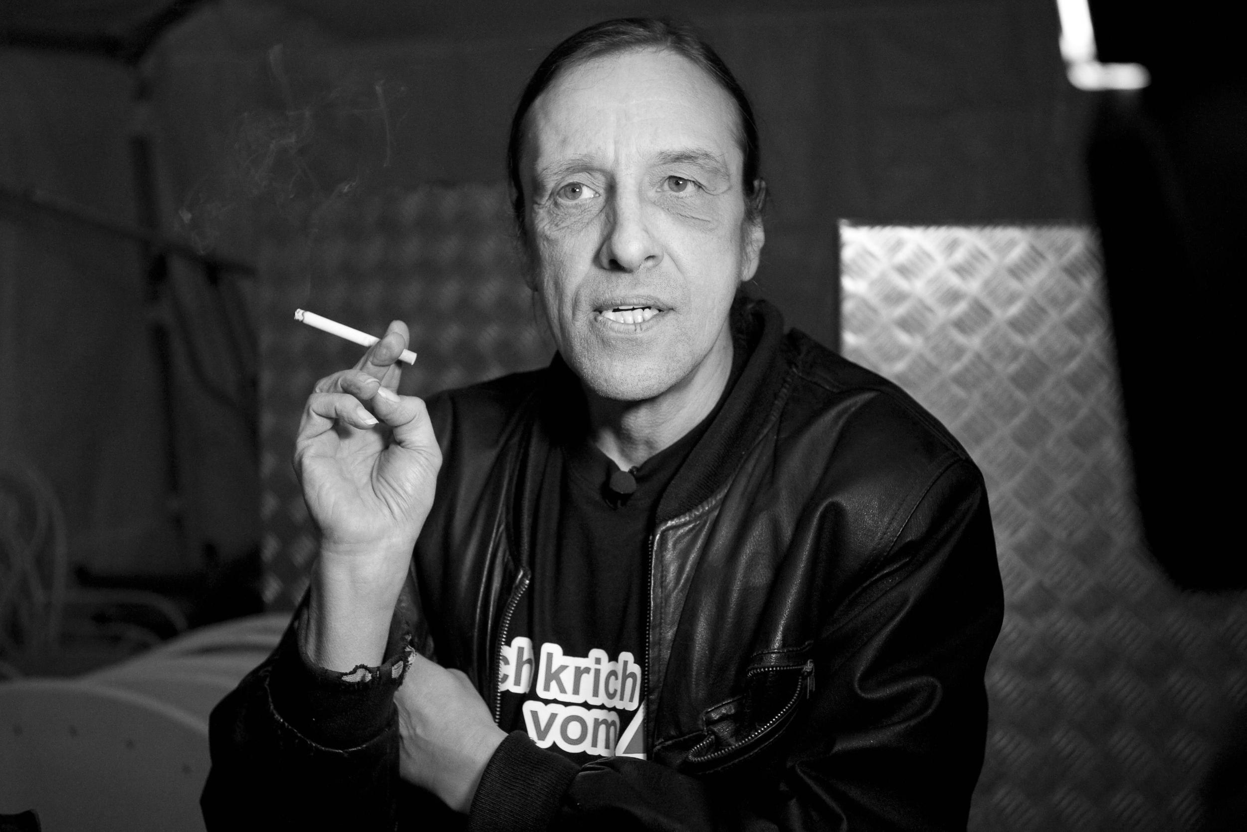 Ein Schwarzweiß-Foto von Arno Dübel. Auf seinem Shirt steht „Ich krich vom Amt“, er hält eine Zigarette in der Hand