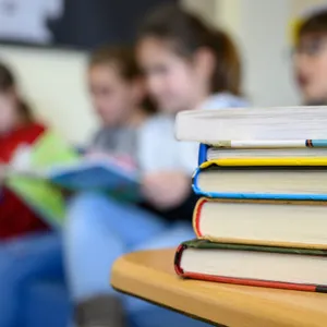 Ein Bücherstapel im Vordergrund, lesende Kinder im Hintergrund.