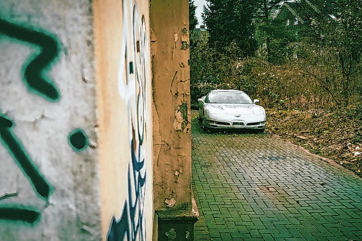 Eine verlassene Corvette steht neben dem baufälligen Haus.