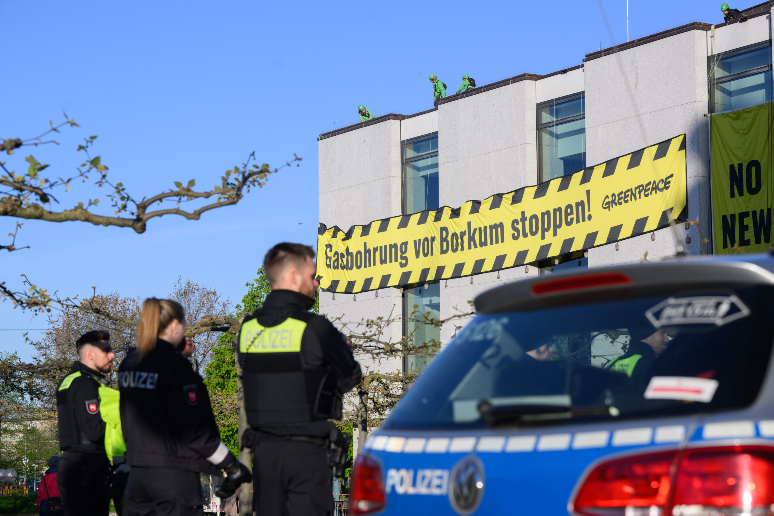 Polizisten beobachten Aktivisten, die gelb- schwarzen Banner mit der Aufschrift „Gasbohrung vor Borkum stoppen!“ an einem Gebäude aufgehängt haben.