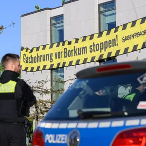 Polizisten beobachten Aktivisten, die gelb- schwarzen Banner mit der Aufschrift „Gasbohrung vor Borkum stoppen!“ an einem Gebäude aufgehängt haben.
