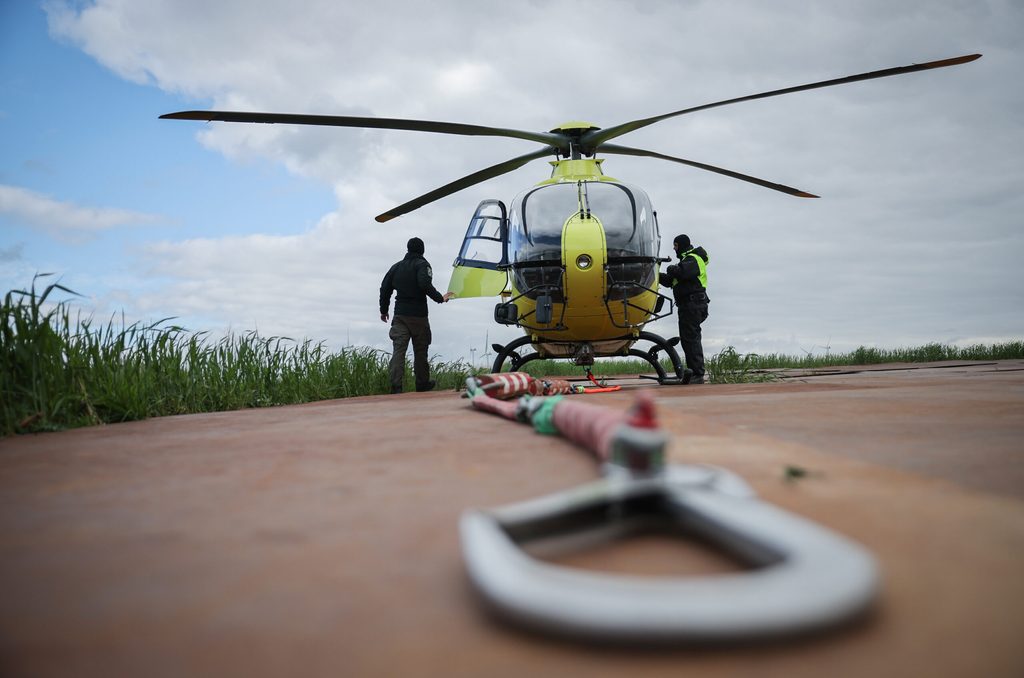 Zwei Personen stehen bei einem gelben Hubschrauber auf einem freien Feld