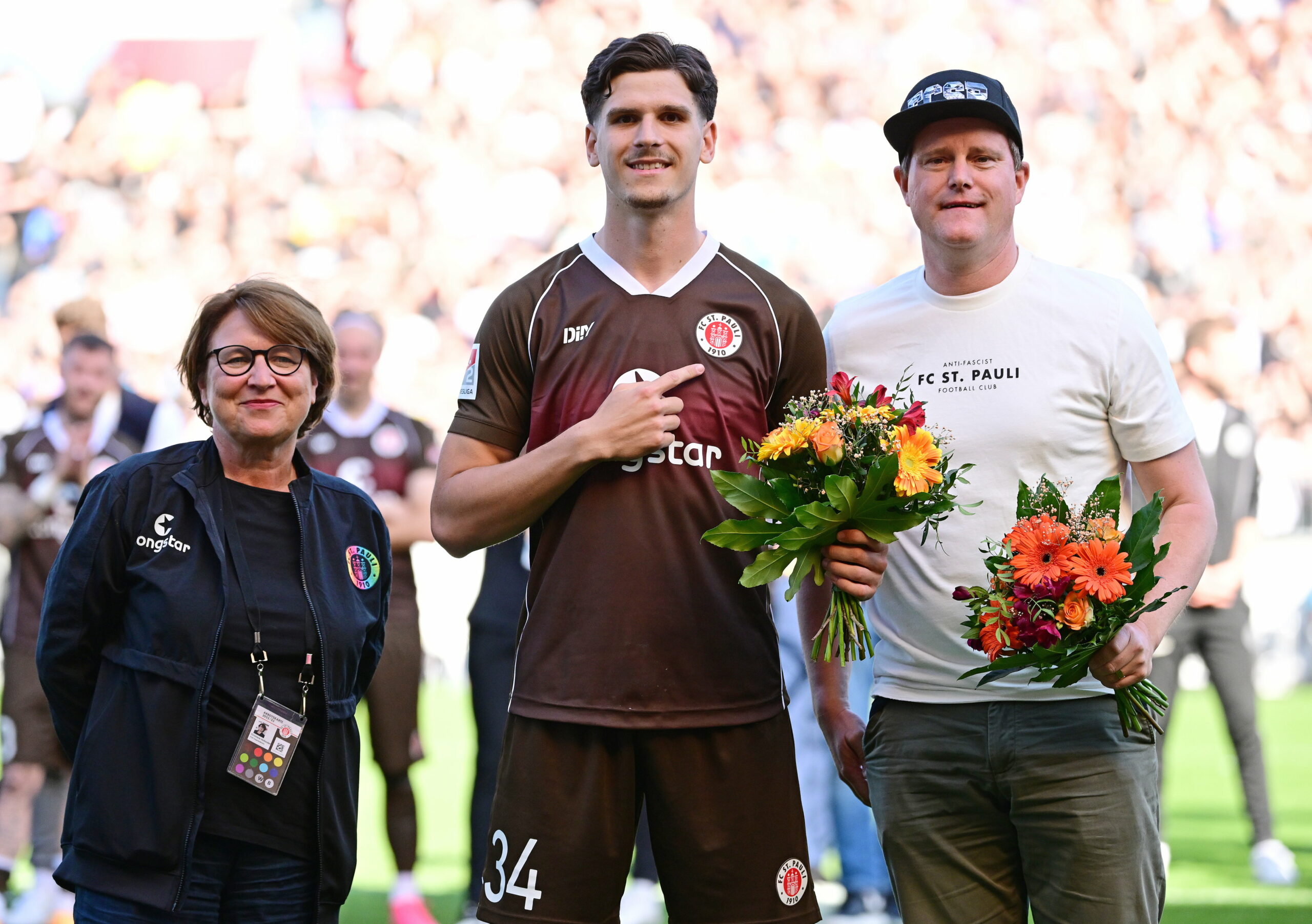 Igor Matanovic weist auf das St. Pauli-Logo, daneben Oke Göttlich, beide mit Blumenstrauß.