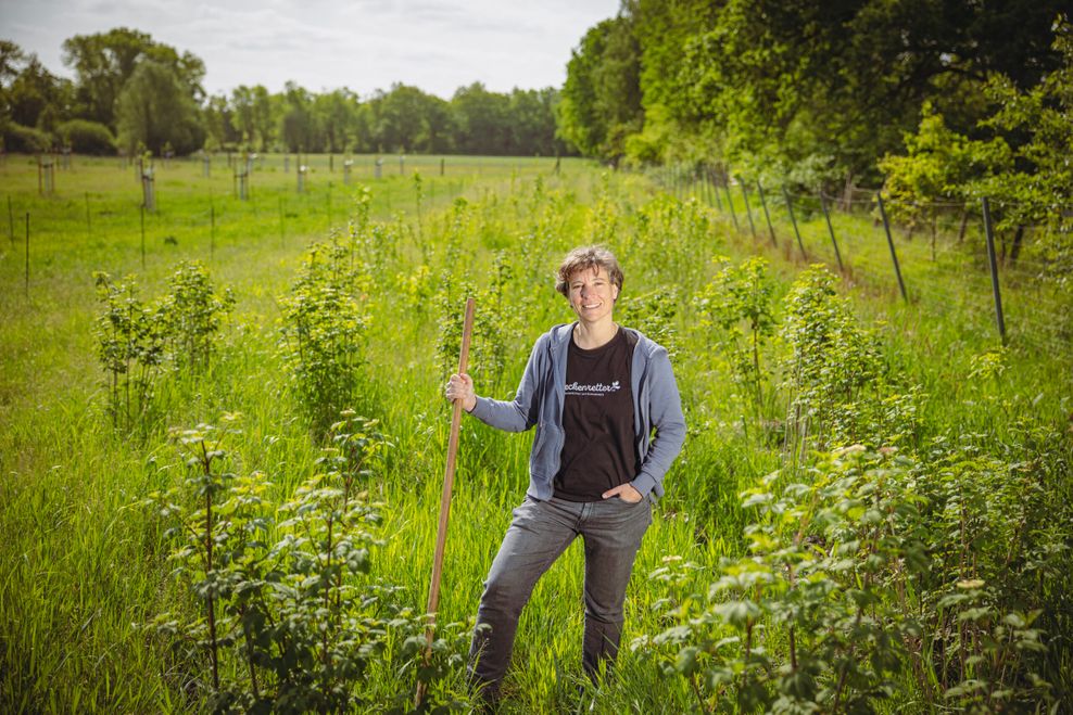 Alexandra mit einem Holzstab in der Hand auf einer Wildheckenwiese