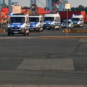 Zahlreiche Polizeifahrzeuge fahren vom Gelände des Container-Terminals.