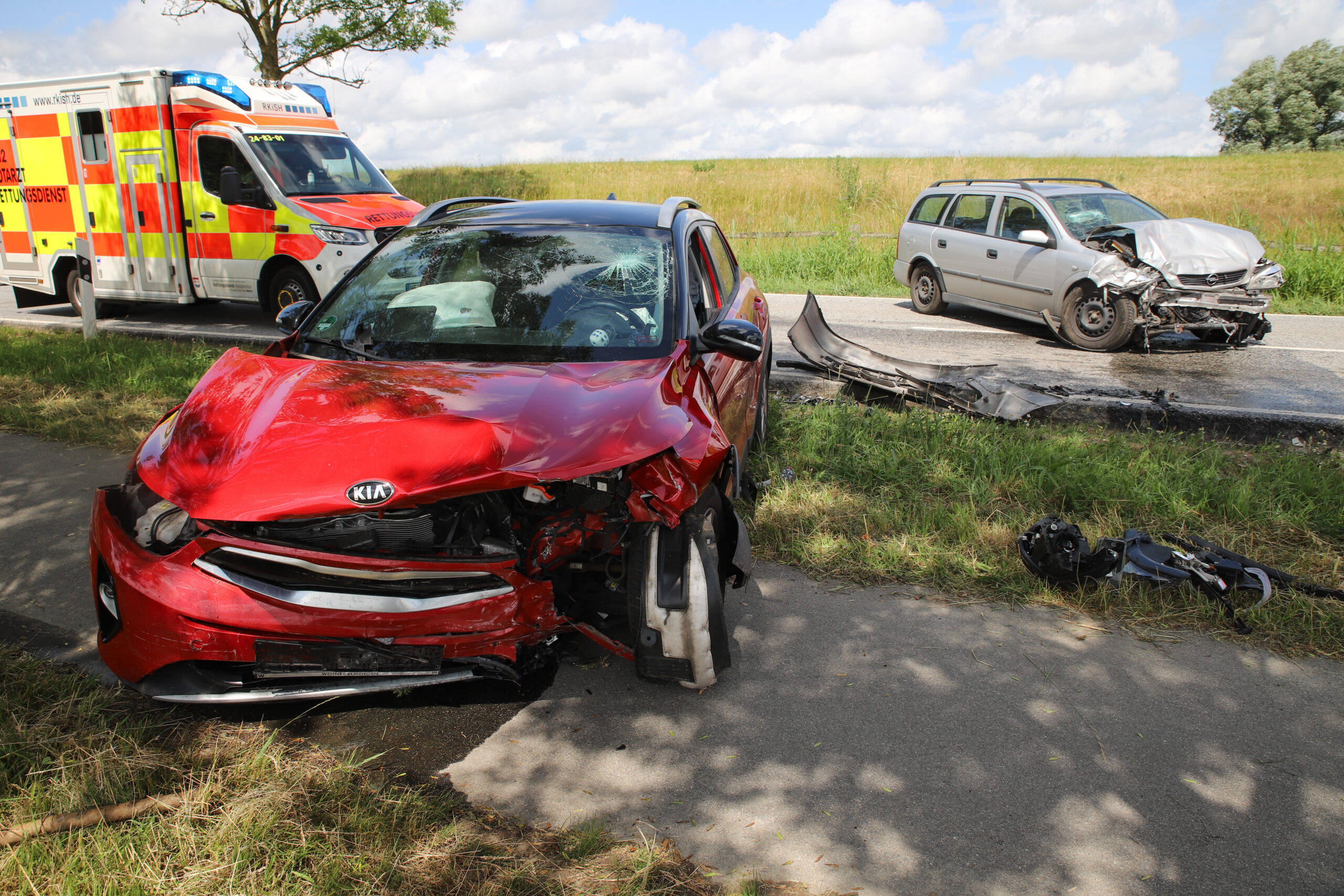 Aufnahme der zerstörten Unfallfahrzeuge, dazu ein Retungswagen im Hintergrund.