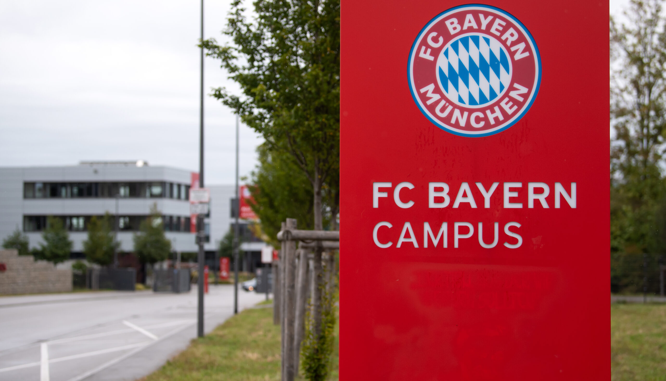 Ein rotes Schild mit der Aufschrift FC Bayern Campus und Logo bei der Einfahrt.