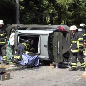 Ein silberfarbener Skoda liegt auf der Seite, Feuerwehrleute befreien den Fahrer.