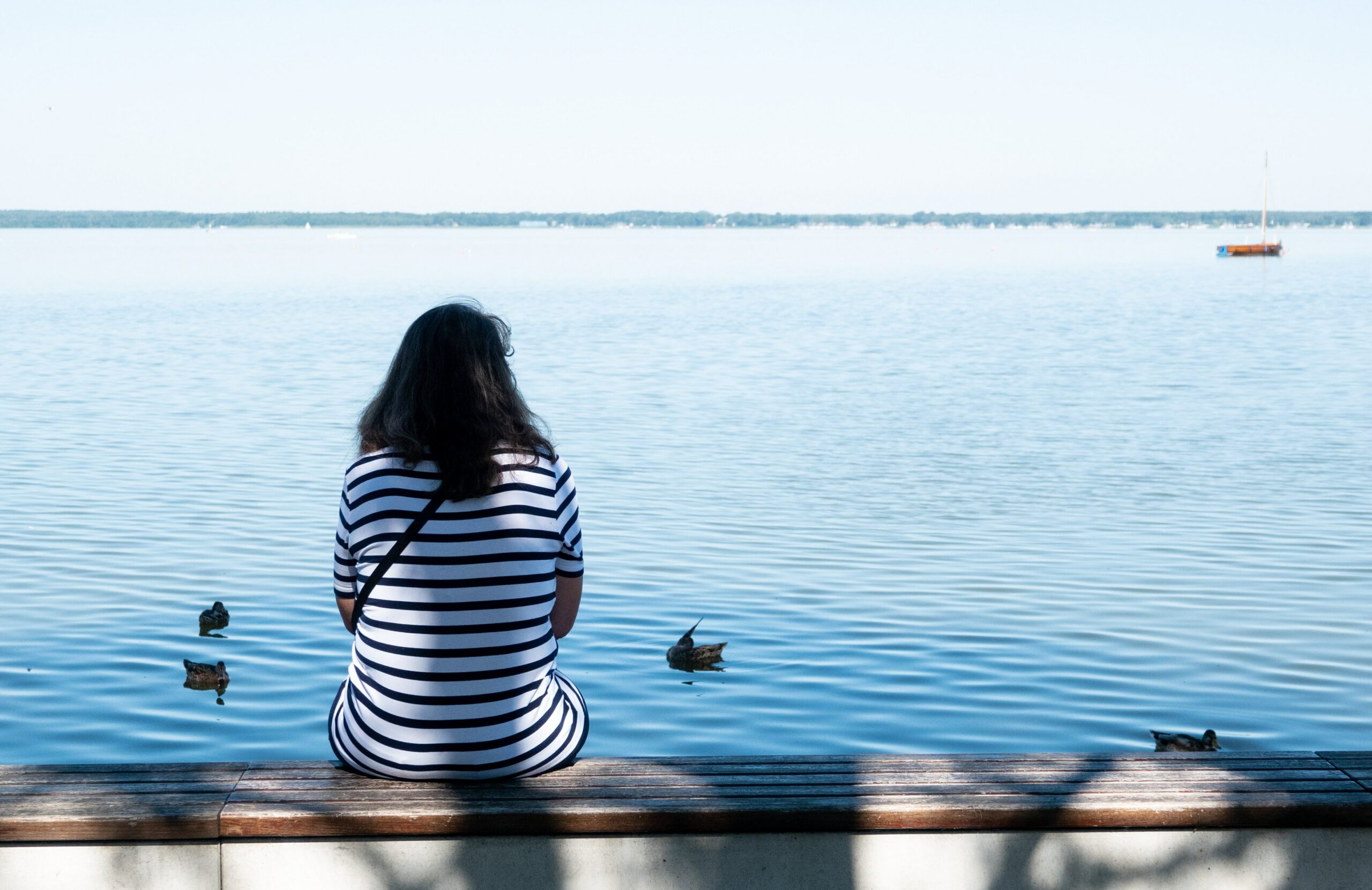 Frau sitz alleine am Ufer eines Sees