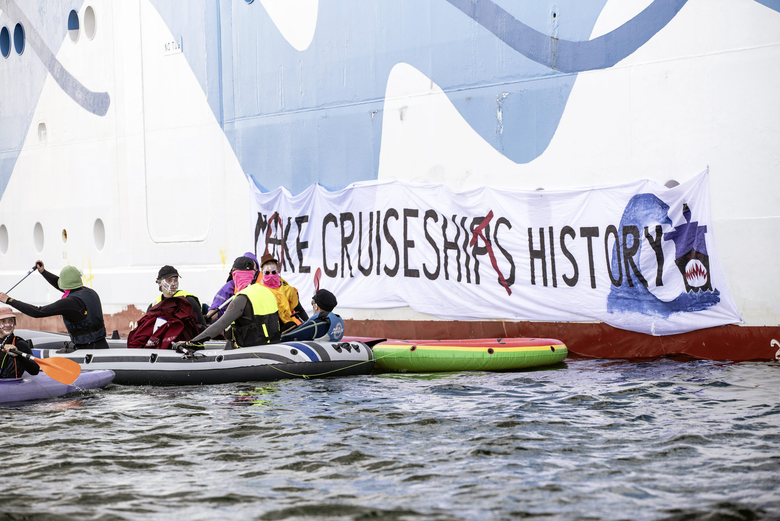 Klimaaktivist:innen versuchen in Rostock-Warnemünde auf Kanus und aufblasbaren Booten ein Kreuzfahrtschiff am Auslaufen zu hindern.