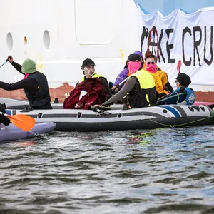 Klimaaktivist:innen versuchen in Rostock-Warnemünde auf Kanus und aufblasbaren Booten ein Kreuzfahrtschiff am Auslaufen zu hindern.