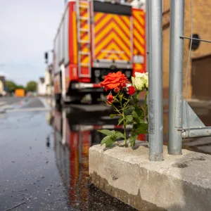 Blumen stehen am Absperrgitter in der Nähe der Brandstelle, wo am vergangenen Sonntag zwei Feuerwehrleute tödlich verunglückten.