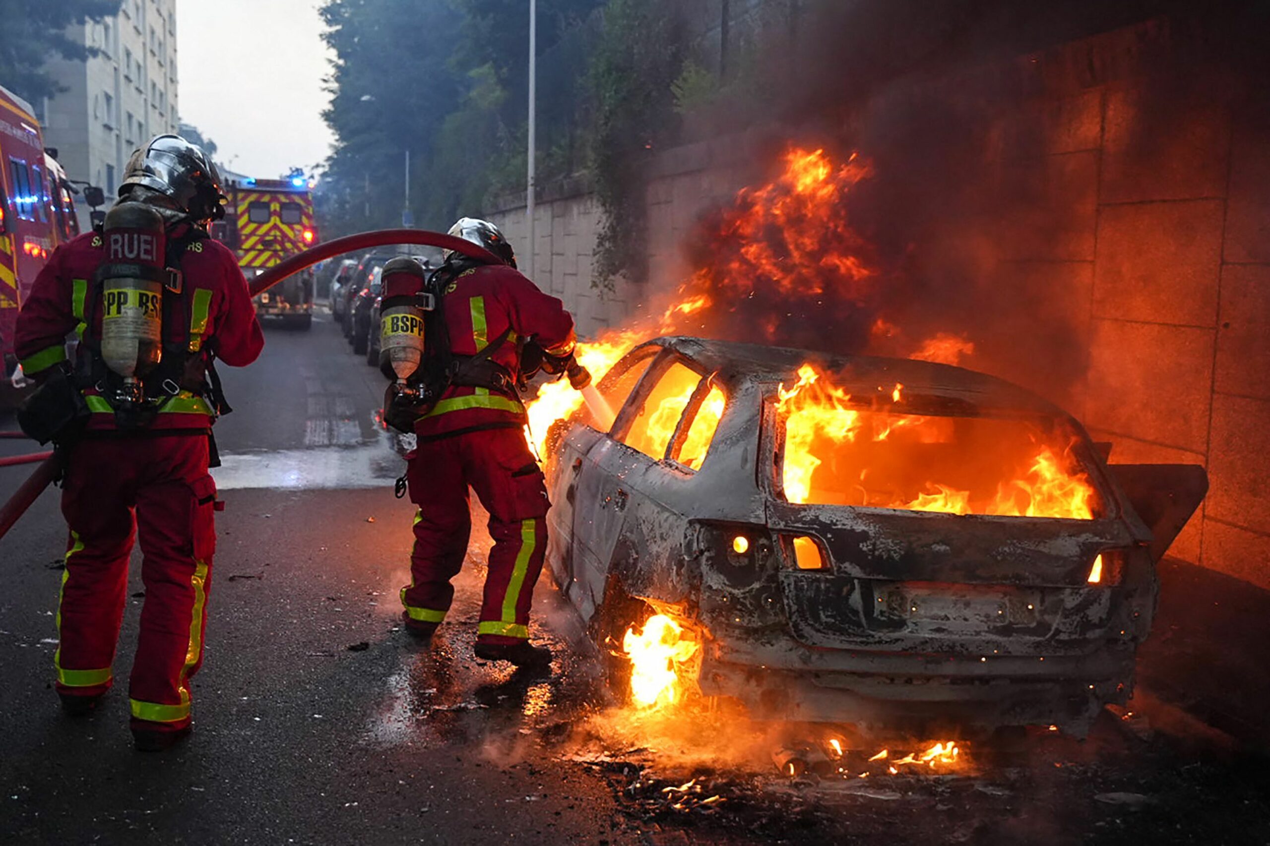 Feuerwehrleute löschen ein brennendes Auto am Rande von Ausschreitungen westlich von Paris.