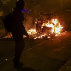Ein Polizeibeamter betrachtet ein brennendes Auto bei Ausschreitungen im Pariser Vorort Nanterre.