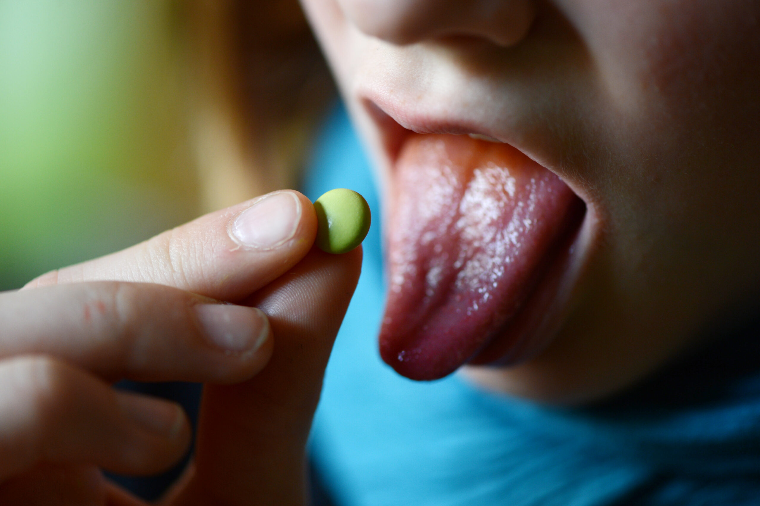 Eine Person mit ausgestreckter Zunge hällt eine Pille in der Hand. Bereit sie zu essen