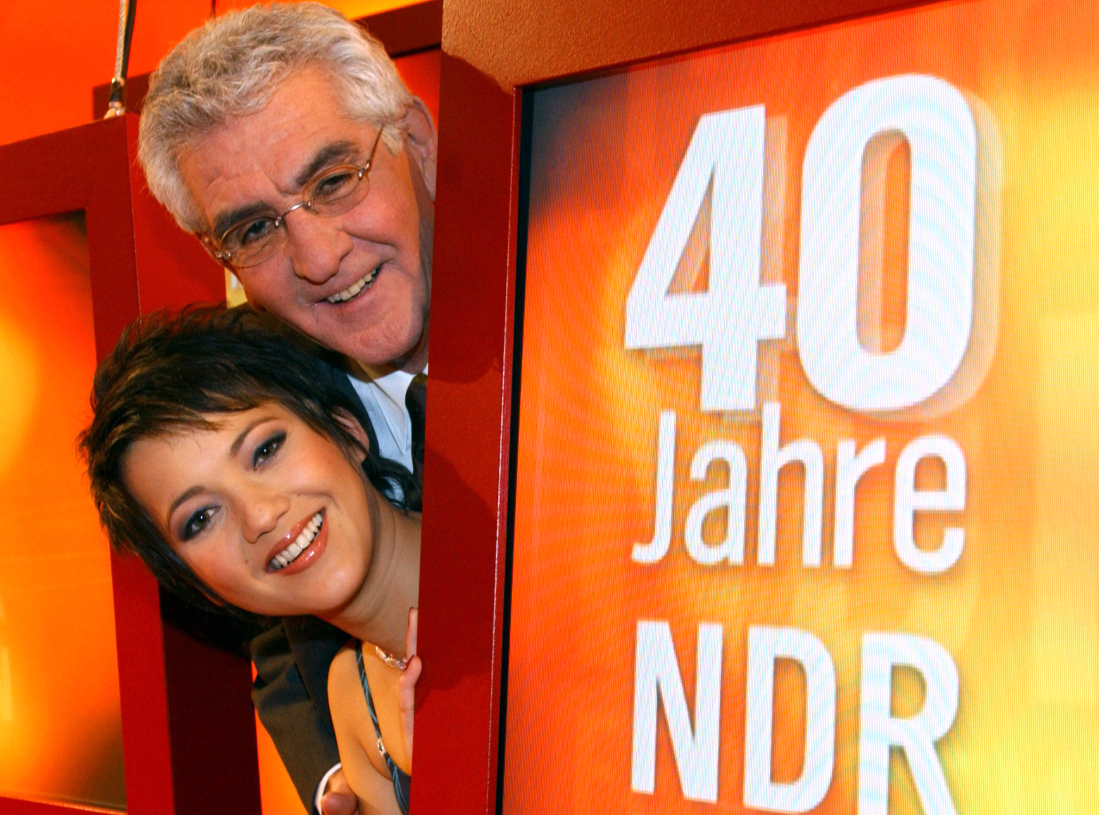 Madeleine Wehle und Denes Törzs blicken lachend hinter einen NDR-Schild hervor (Archivbild)