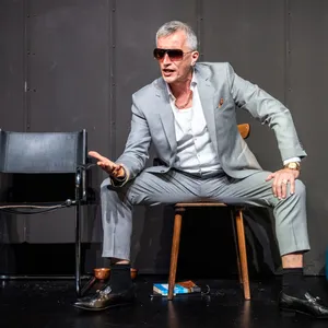 Typ sitzt mit breiten Beinen, dicker Uhr und Sonnenbrille unangenehm auf einem Stuhl