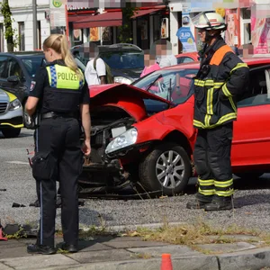 Feuerwehrleute und eine Polizistin stehen neben einem der beiden Unfallautos.