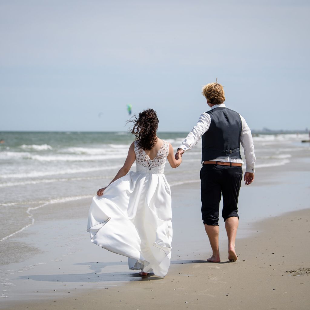 Ein Brautpaar geht nach der Trauung am Strand von Juist entlang.