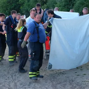 Rettungskräfte von Polizei und Feuerwehr sowie freiwillige Helfer sind am Seeufer im Einsatz.