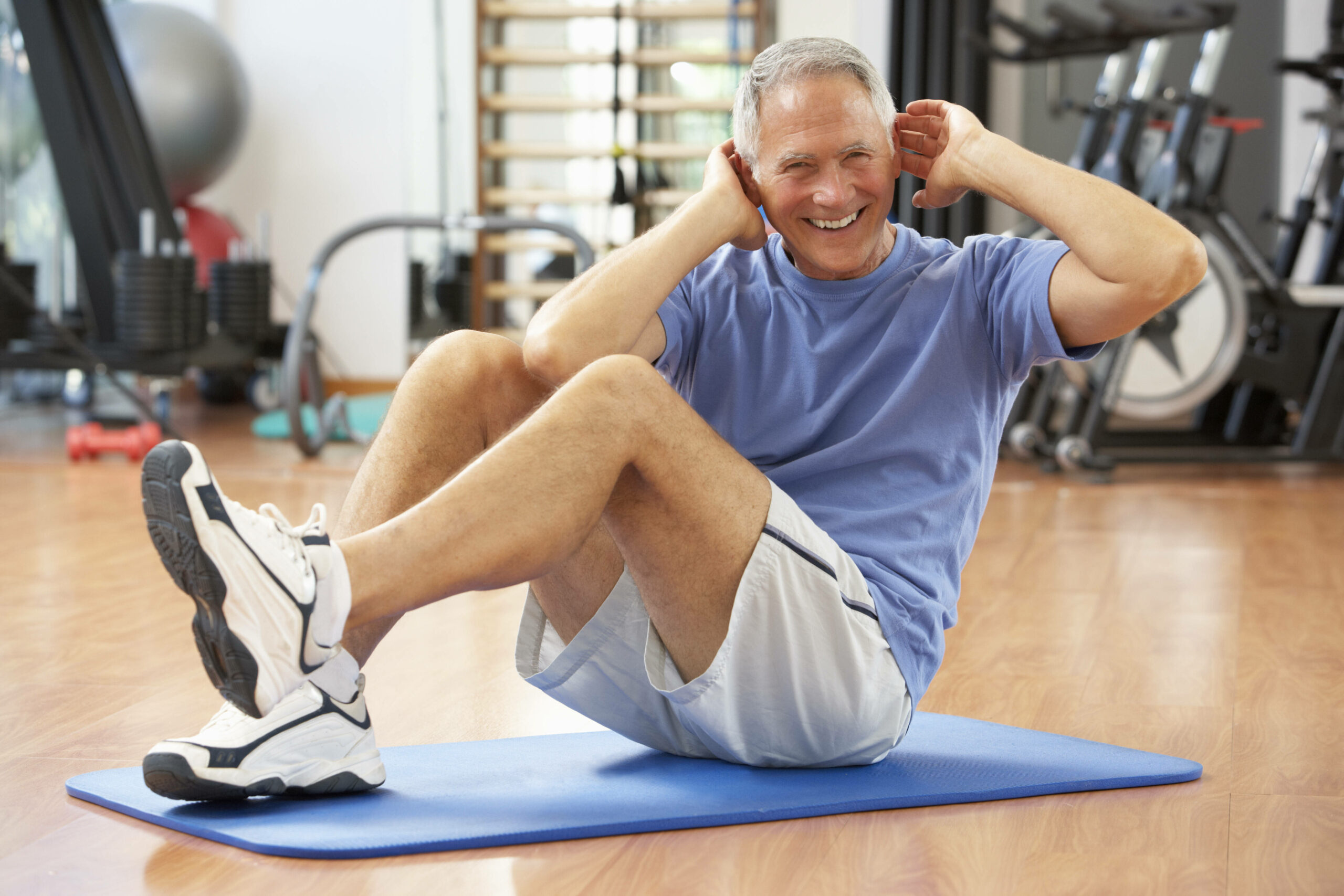 Älterer Mann der auf einer Yogamatte mit den Händen am Kopf lächelnd eine Sportübung ausführt