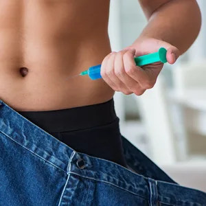 Mann benutzt Abnehmspritze und trägt eine zu große Hose, die Übergewicht symbolisieren soll. (Symbolbild)